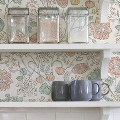 three mugs are sitting on a shelf with floral wallpaper