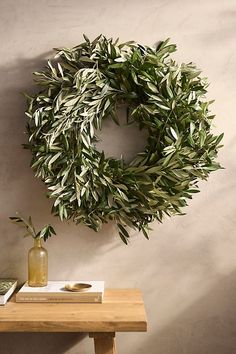 an olive wreath hangs on the wall next to a table with books and vases