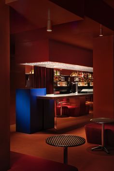 an empty bar with stools and tables in the center, lit by red lights