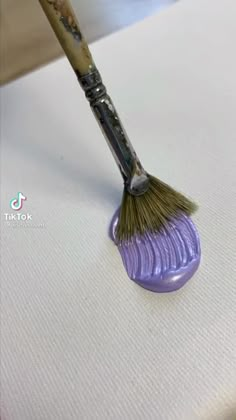 a purple brush sitting on top of a white surface next to a small round object