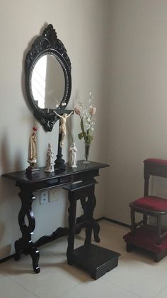 a small table with a mirror on it next to a red chair and flower vase