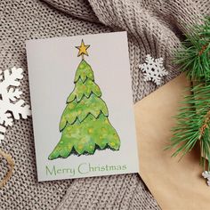 a card with a christmas tree on it next to snowflakes and pine branches