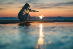 a woman kneeling down on the ground with a sparkler in her hand at sunset