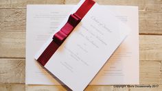 a wedding card with a red ribbon on top of it next to a piece of paper