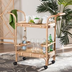 a bamboo serving cart with drinks and glasses on it in front of a potted plant