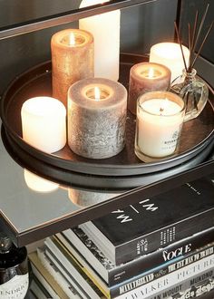 some candles are sitting on a black tray near books and a candle holder with three burning candles in it