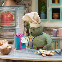 a teddy bear with a chef's hat on sitting at a table next to a gift box