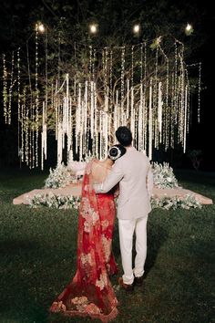 a bride and groom standing in front of a tree with white lights hanging from it