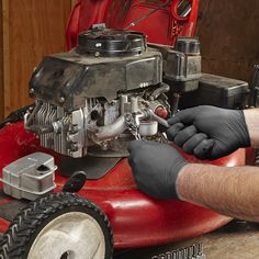 a man in black gloves working on a red lawn mower