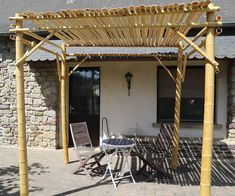 a patio with chairs and a table under a pergolated arbor in front of a house