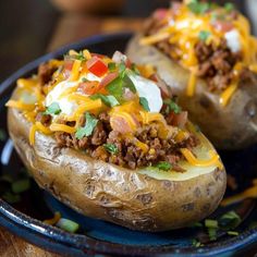 two loaded baked potatoes on a plate with cheese and other toppings, ready to be eaten