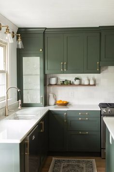 a kitchen with dark green cabinets and white counter tops, gold pulls on the handles