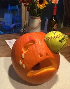 an orange pumpkin with a baseball on it's head and flowers in a vase