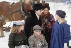 three women and two children standing in the snow with some horses behind them on a snowy day