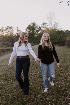 two women holding hands and walking through the grass