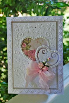 a white card with a pink bow and heart on the front, sitting on top of a table