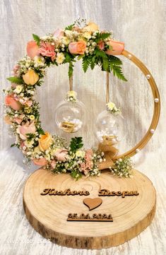 an arrangement of flowers and greenery is arranged on a wooden stand with two wine glasses