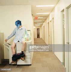 a man sitting on top of a filing cabinet in an office hallway wearing a blue bandana