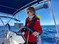 a woman on a sailboat in the middle of the ocean with her hand on the steering wheel