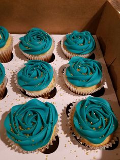 cupcakes with blue frosting and gold sprinkles in a box