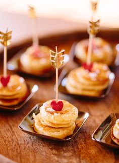 small pancakes with strawberries on top are arranged on tiny trays in the shape of hearts