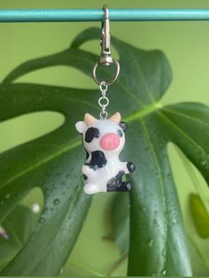 a keychain with a cow on it is hanging from a green plant leaf