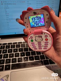 a person holding up a hello kitty cell phone in front of a laptop computer screen