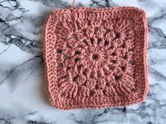 a pink crocheted square sitting on top of a marble counter next to a string