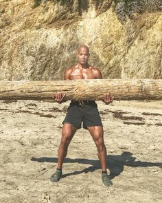 a man is holding a large log on the beach