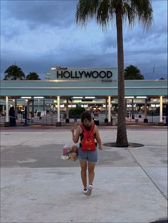 a woman with a red backpack is walking towards the hollywood sign and palm trees in front of her