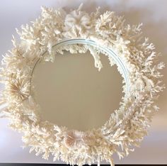 a white wreath is hanging on the wall in front of a mirror that has been decorated with seashells