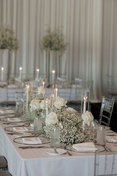 the table is set with white flowers, candles and place settings for an elegant dinner