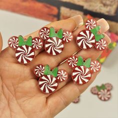 a hand is holding six candy canes with green leaves on them in front of some candies