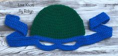 a crocheted hat with blue and green ribbon on it, sitting on top of a wooden table