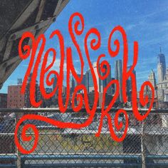 the word hello kitty is written in red ink on a fence with cityscape behind it