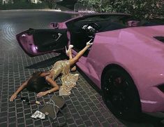 a woman laying on the ground next to a pink sports car