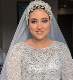 a woman wearing a wedding veil with pearls on the head and shoulders, smiling at the camera