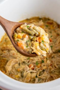 a wooden spoon full of soup with chicken and veggies in it, on top of a white bowl