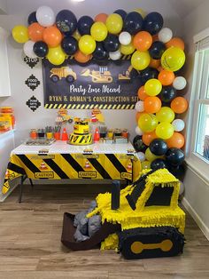 a construction themed birthday party with yellow and black balloons on the wall, cake table