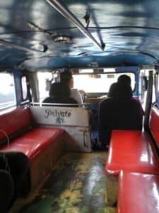 two people sitting in the back of a bus with red seats on each seat and one person standing at the front