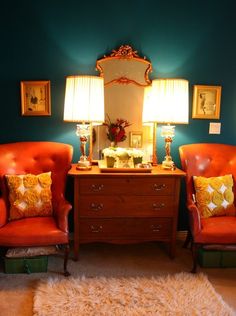 two orange chairs sitting next to each other in front of a dresser with lamps on it