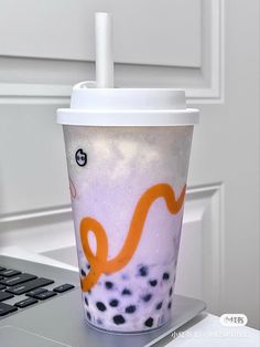 a coffee cup with an orange snake painted on it sitting in front of a laptop