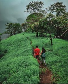 two people are walking up a grassy hill