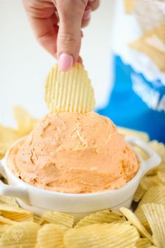 a hand holding a chip over a bowl of chips with the dip in it's center