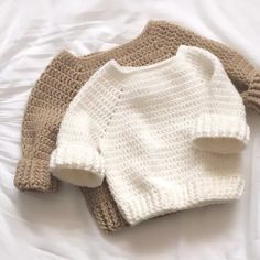 two knitted sweaters laying on top of a white bed next to each other