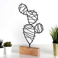 a wire sculpture sitting on top of a wooden block next to potted cacti