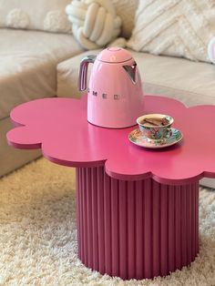 a pink coffee table with a tea pot on top and a plate in the middle