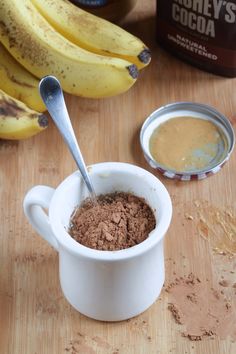 a cup filled with cocoa next to some bananas and other ingredients on a wooden table