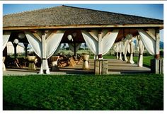 a gazebo with white drapes on the roof and grass in front of it