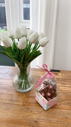 white tulips are in a vase next to a box of chocolate candies